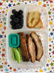 Photo of a bento box lunch filled with ribs, sugar snap peas, berries and garlic bread